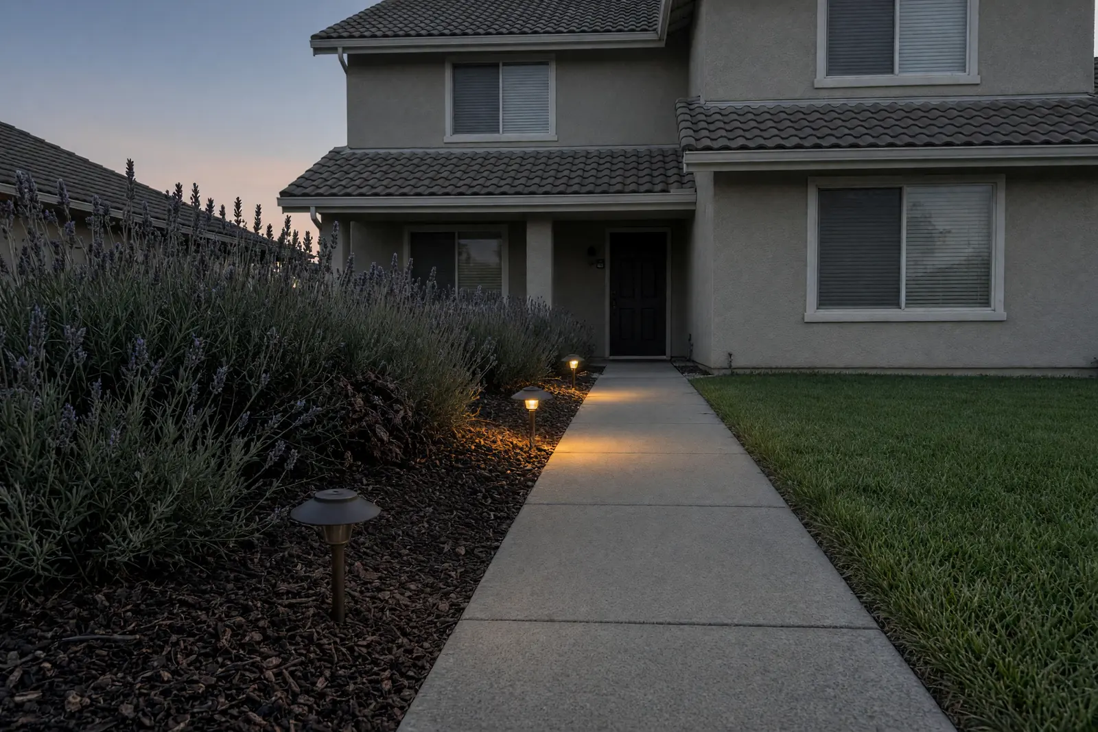 Illustration: path lights along a front walk at dusk, two glowing and the nearest one dark, beside an overgrown lavender.