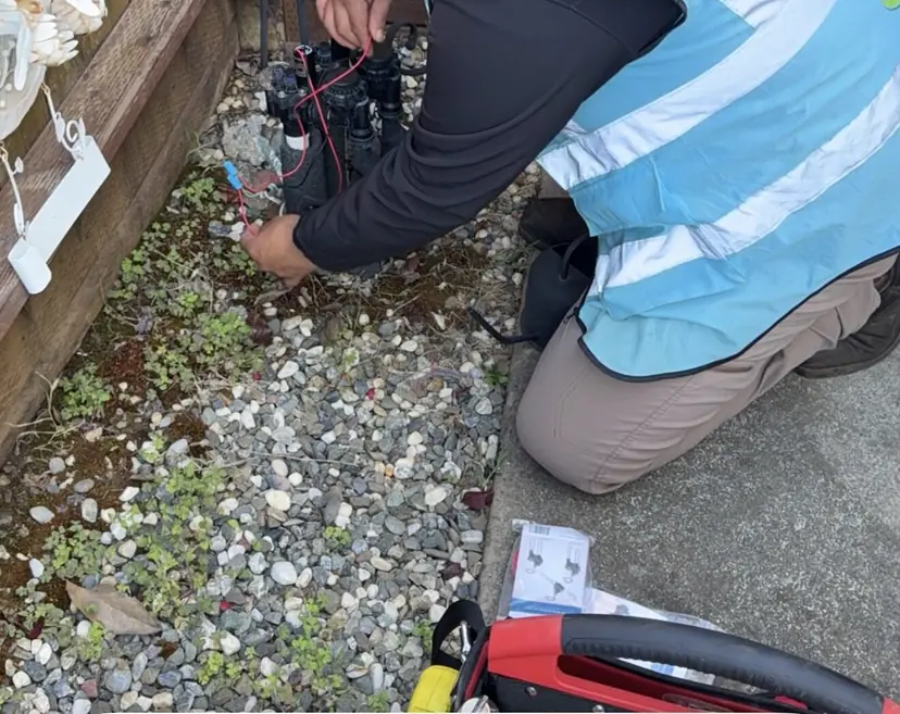 Eco Scapes technician wiring a sprinkler valve manifold in a gravel side yard next to a wood fence
