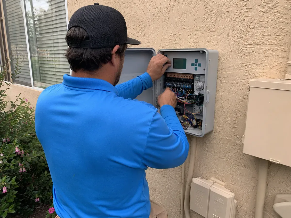 Technician replacing sprinkler controller on a garage wall with wiring visible in California